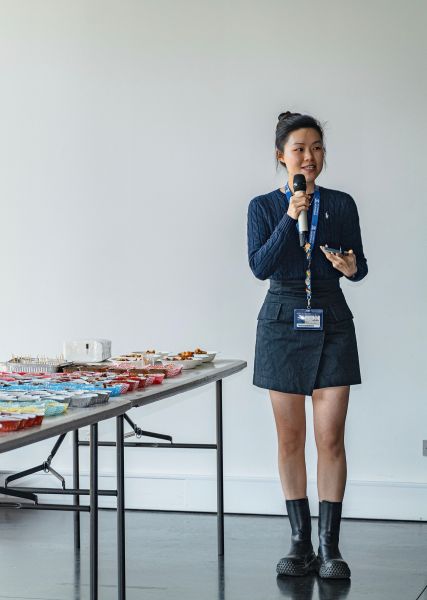 Wanyi standing holding a microphone, next to a table of sliced mooncakes.