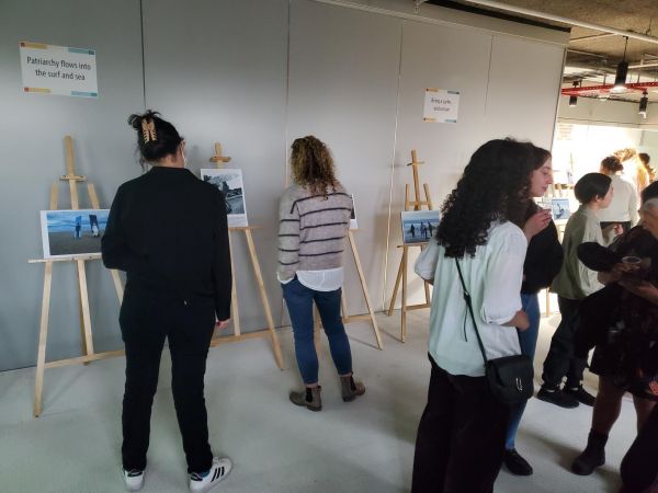 people standing in groups and 2 people looking and reading from the easels of artwork