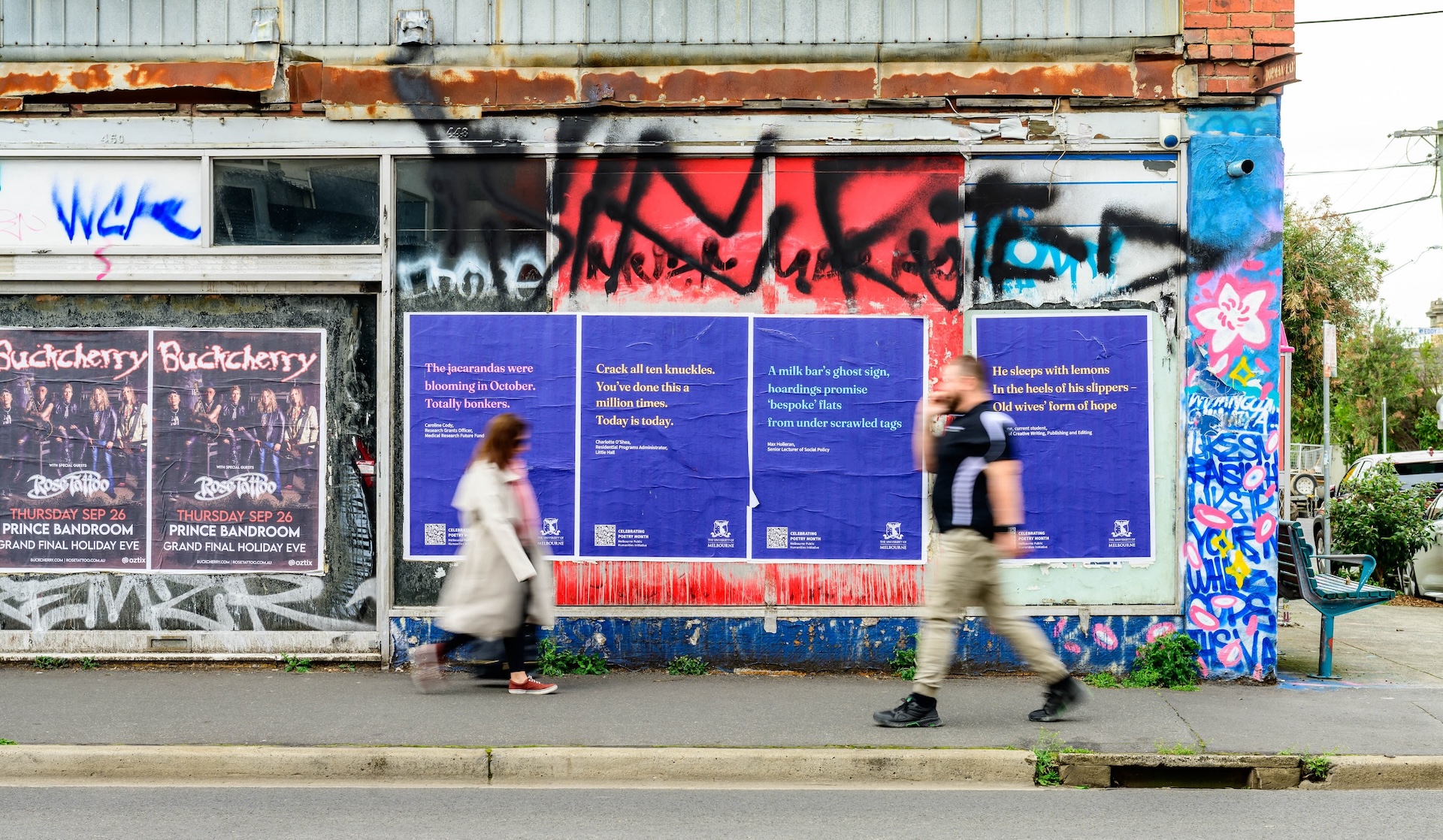 Two people passing each other in a Melbourne street with billboard posters behind them