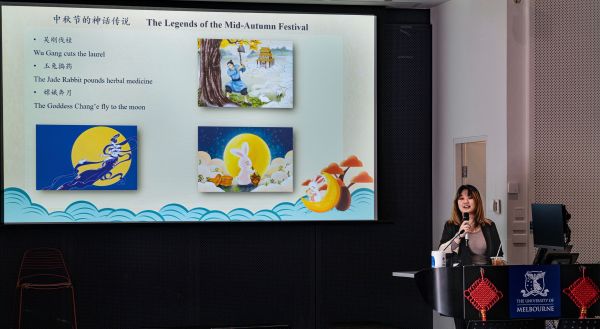 Leiheng speaking into a micrphone in front of a powerpoint slide on the legends of the Mid-Autumn Festival