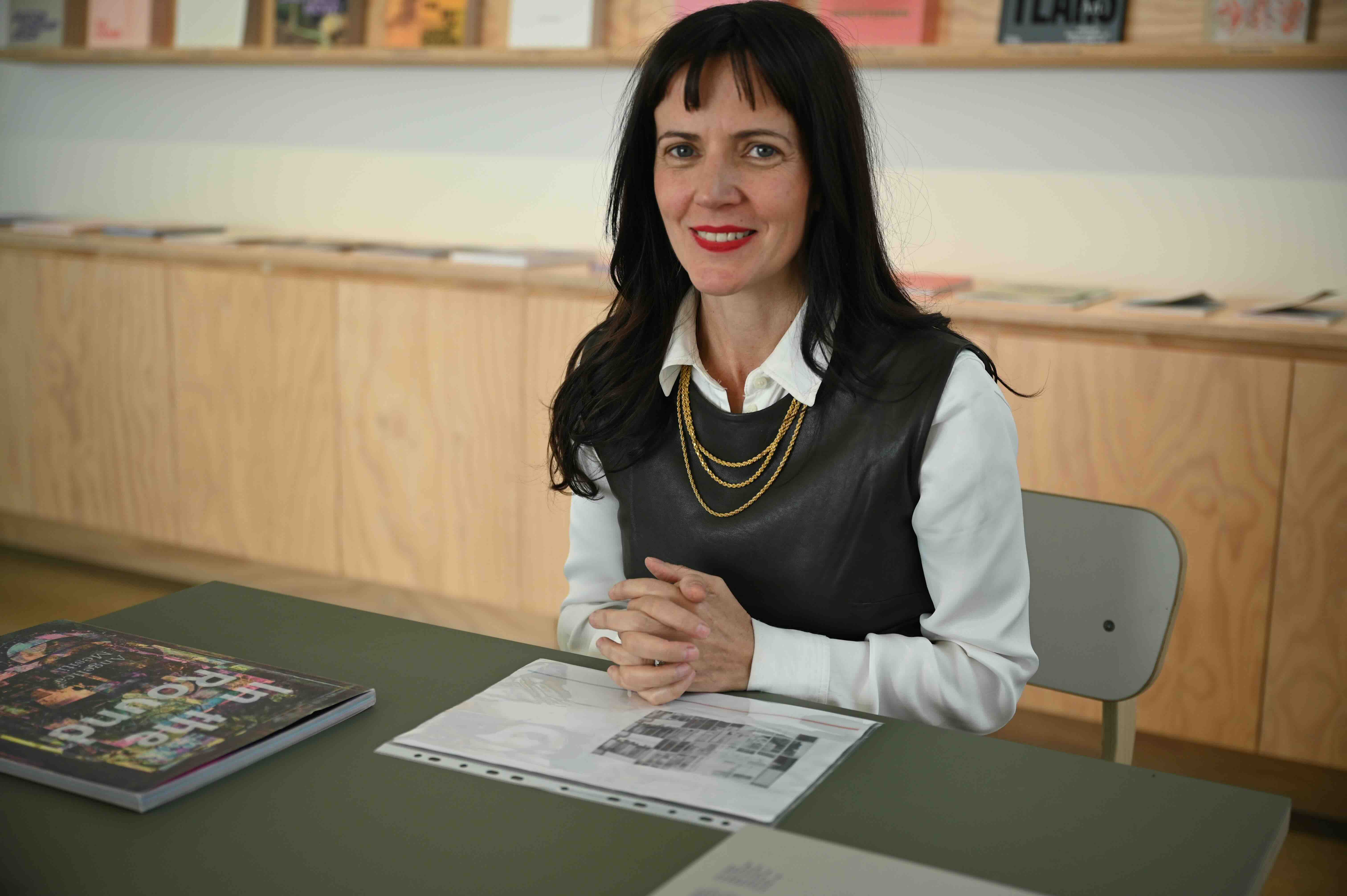 A woman sits in a light-filled gallery smiling