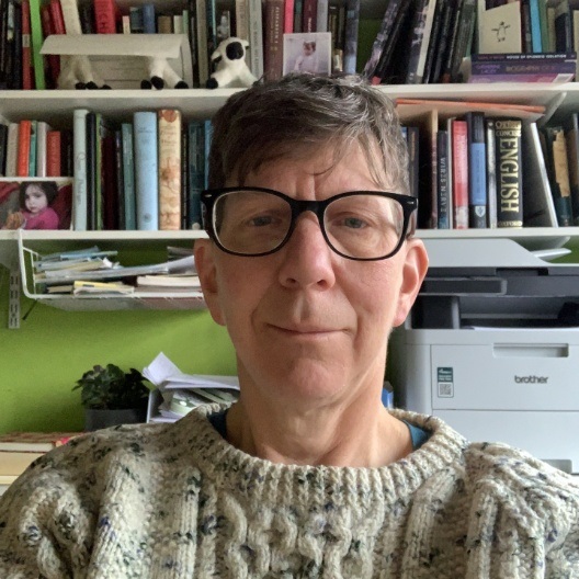 image of person wearing glasses in front of shelves of books