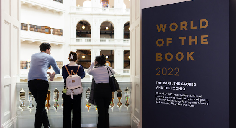 Three visitors to the exhibition lean against the balony on the Library's Dome Reading Room