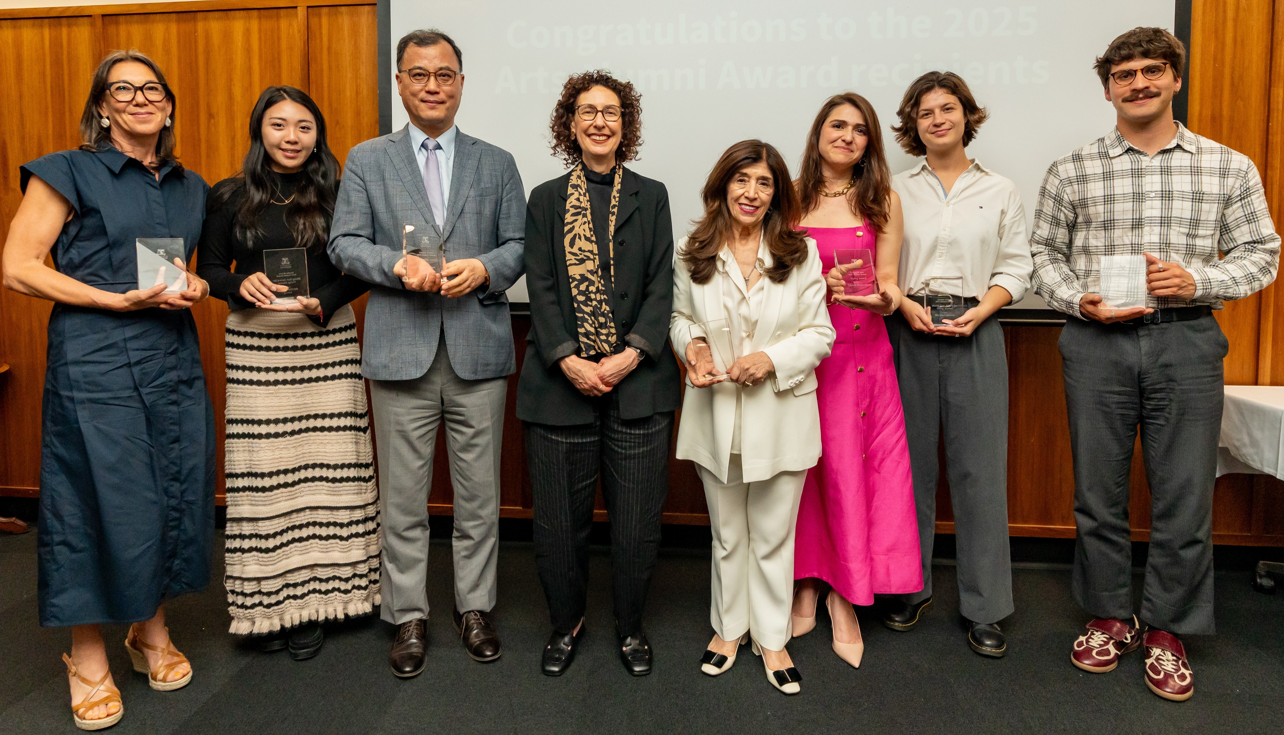 Alumni Award winners standing on stage with the Dean smiling and posing for the photo, holding their glass awards