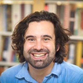 image of man with long brown hair and a beard infront of book shelves