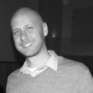 Black and white photgraph of man in grey knit jumper with white collard shirt