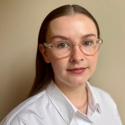 image of Jess Marian, women with glasses and brown hair in front of a beige background