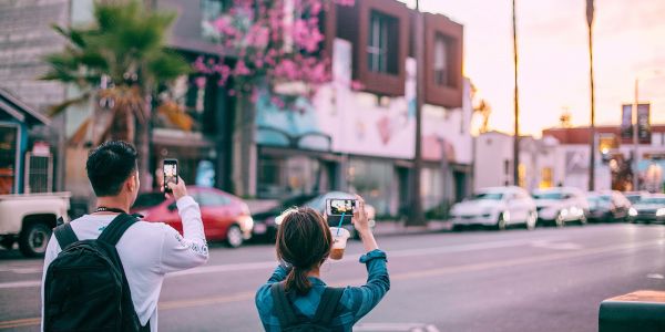 A girl and a boy taking images of a streetscape at sunset on their phones