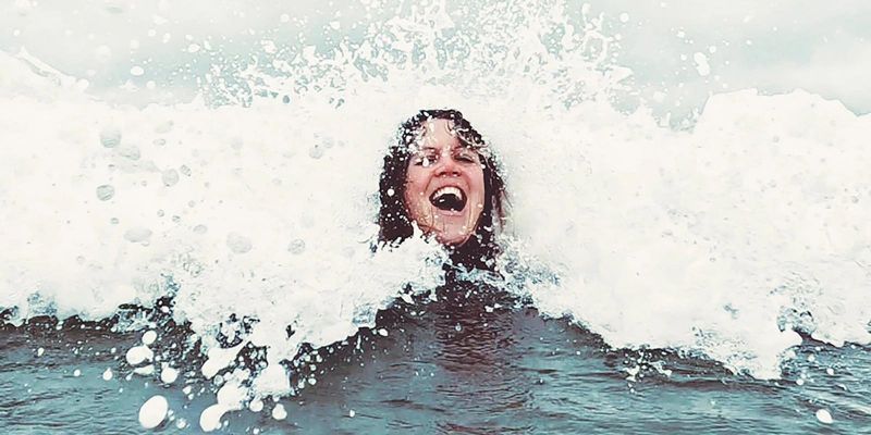 Surfer woman emerging from a wave in the ocean smiling
