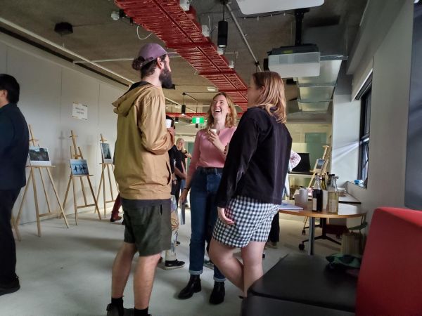 3 people talking in a group surrounded by easels at exhibition