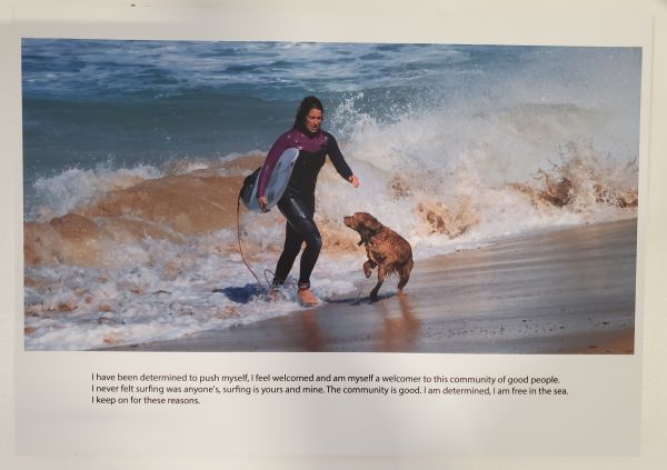 woman in wetsuit holding surfboard coming out of ocean with a golden retriever bounding next to her