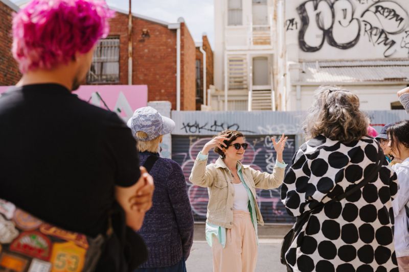 Woman presenting to group in graffitied laneway
