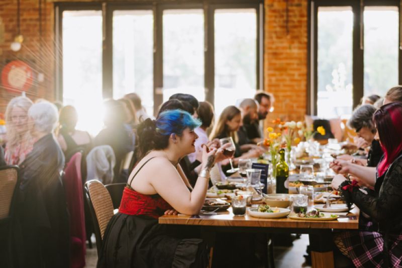 Restaurant full of people at dinner, with girl sitting in foreground wearing red and black dress with blue hair