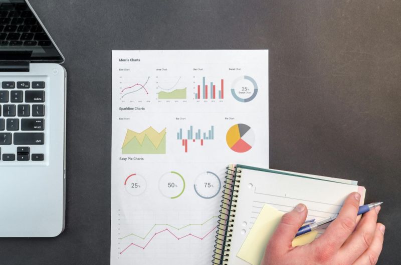A hand holding a notebook and pen with graphs and charts pictured