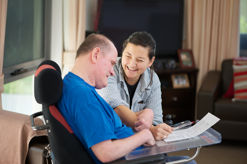 Caregiver and man in a wheelchair smiling while reviewing a document together