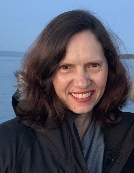 Image of smiling woman with brown hair, wearing a black jacket in front of a body of water 