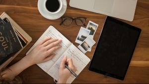 person writing in notebook with laptop near