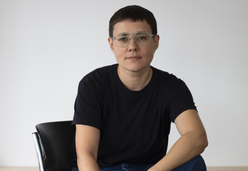 Profile image of Ju Bavyka sitting on a chair with blank background