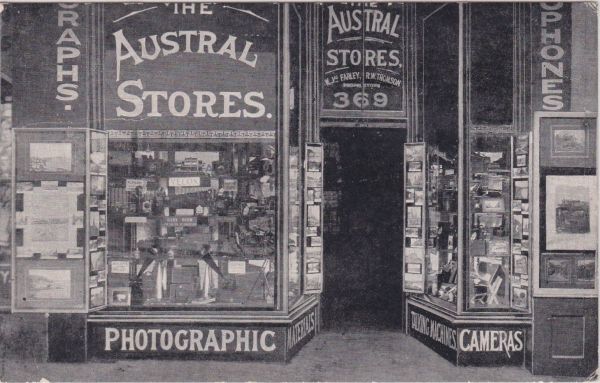 An old photo in black and white of a shop front that reads 'Australian stores' and 'photographic' and 'cameras' across the front.