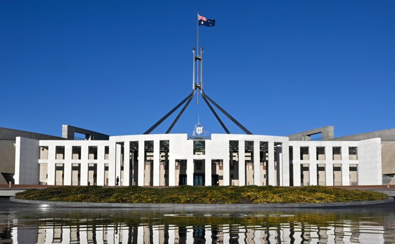 A white building with a flag on top - Parliament House, Canberra