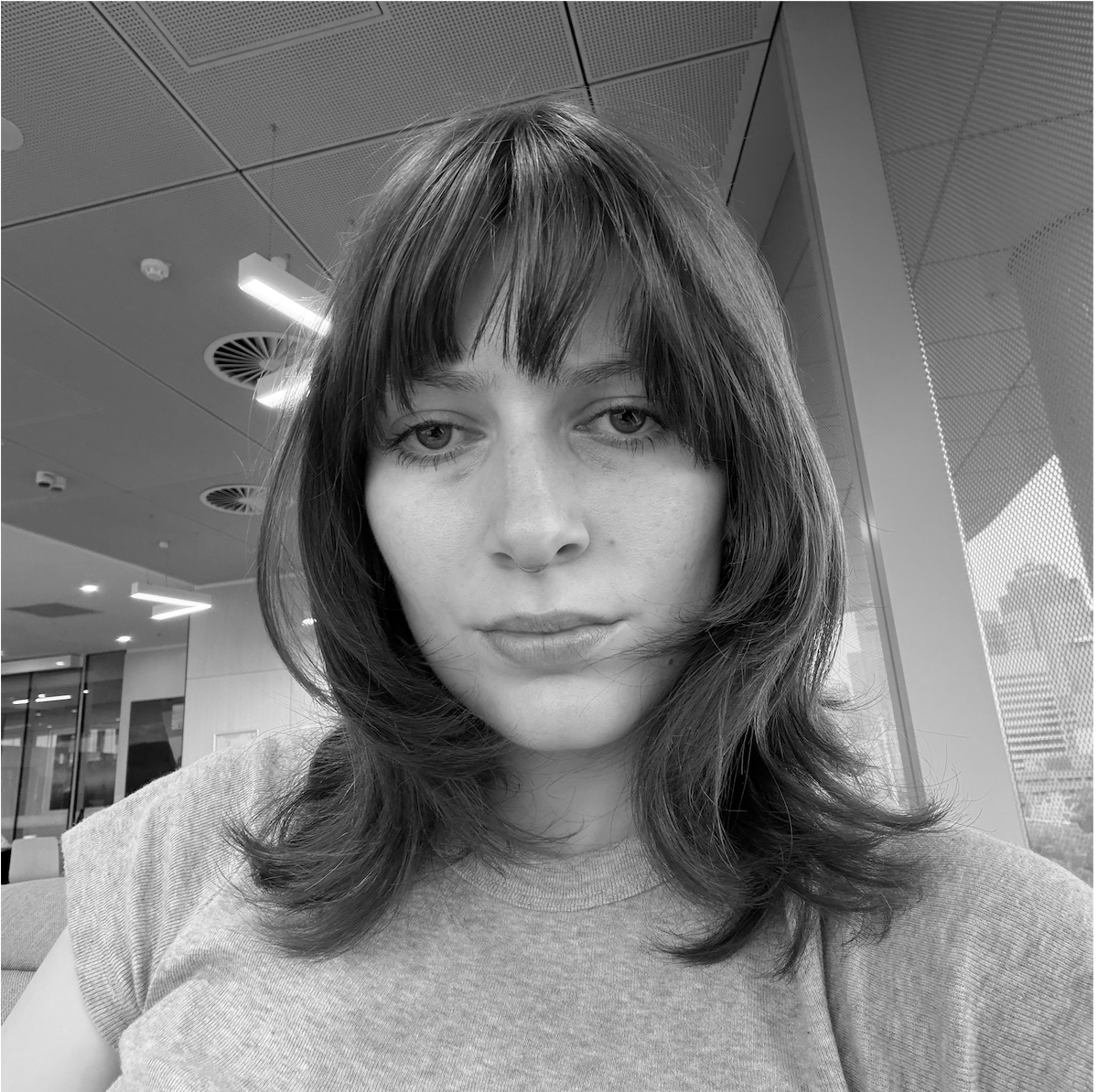 Image shows a black and white photo of a woman's face who has shoulder length dark hair and a fringe