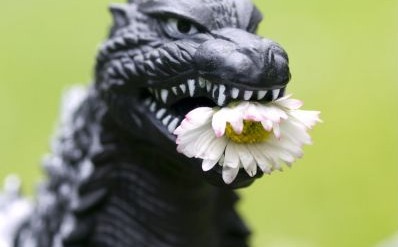A plastic godzilla toy with a flower in its mouth
